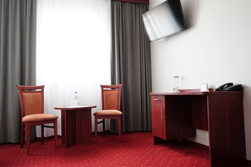 Kącik wypoczynkowy i biurko w hotelu Maraton: dwa krzesła przy okrągłym stoliku, biurko z telefonem i telewizor na ścianie.